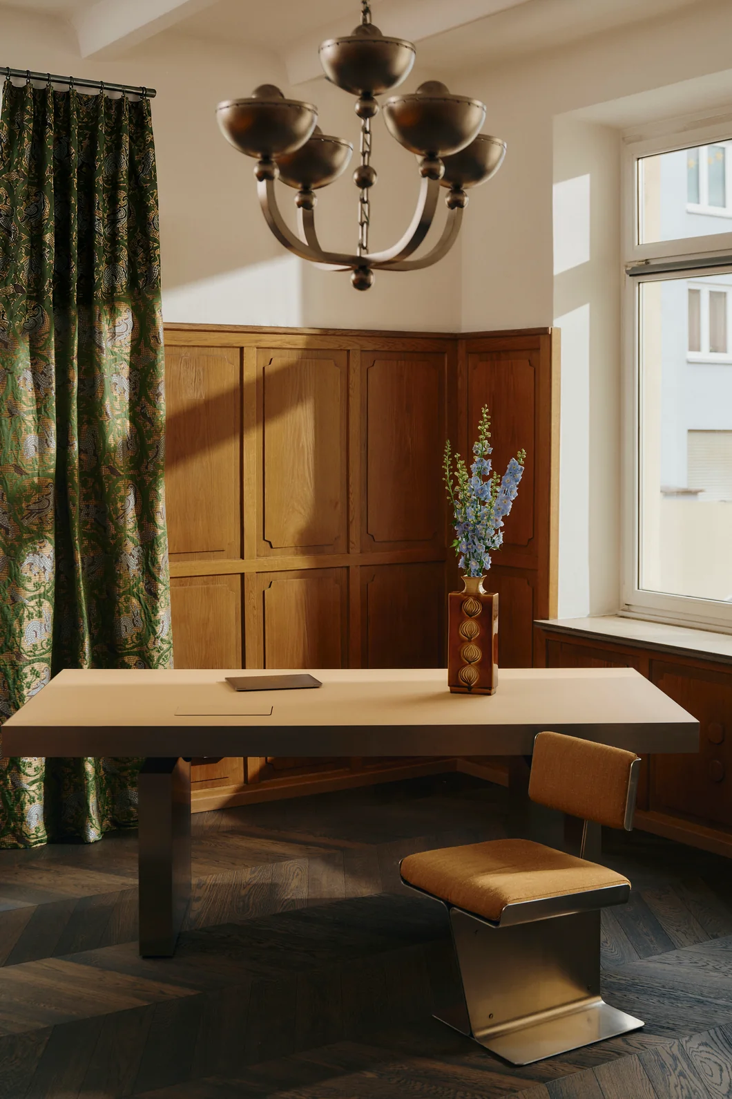 Desk with a leather chair, a brass chandelier and a patterned curtain at Le Comptoir. Photo: Conny Mirbach