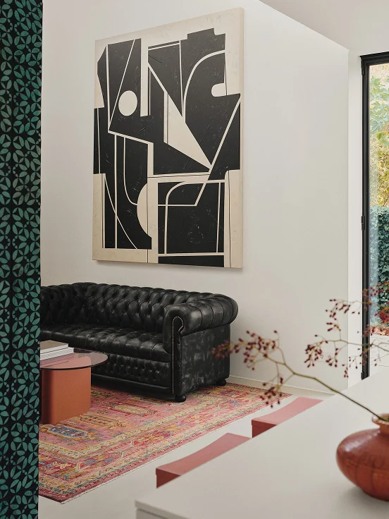 Black and white artwork above a black leather Chesterfield sofa on a red rug.