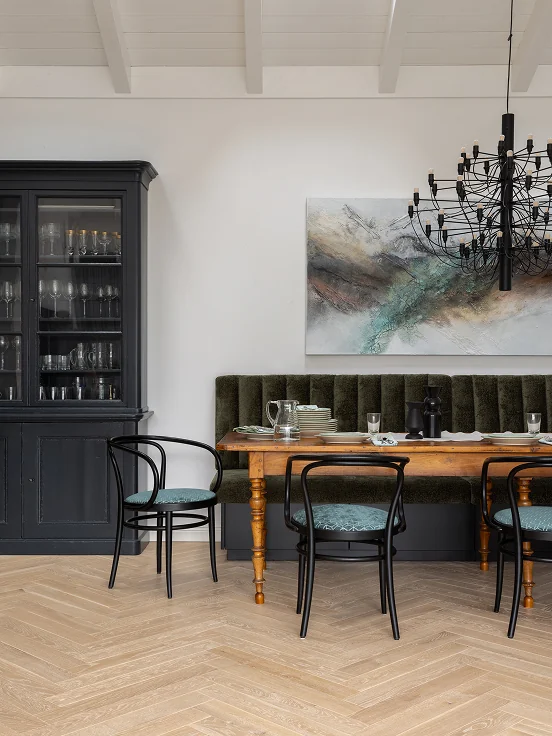 Dining room with a dark glass cabinet, a green velvet bench and a black chandelier.