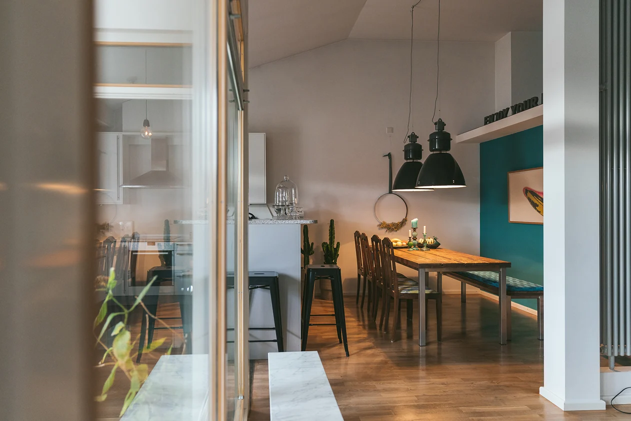 View into an open kitchen and dining area with industrial pendant lights and a petrol blue wall. Photo: Tomo Yarmush