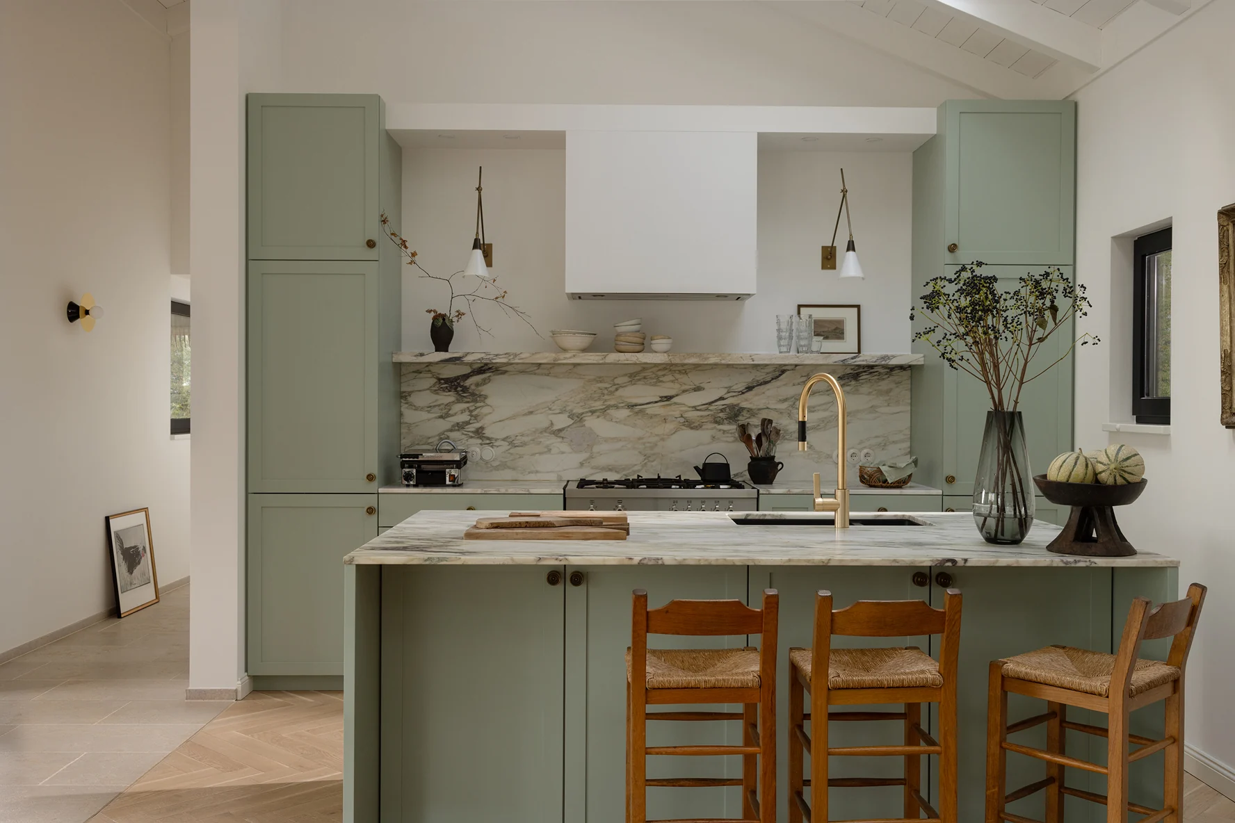 Sage green kitchen with a marble backsplash and rush seat bar stools. Photo: Jordana Schramm
