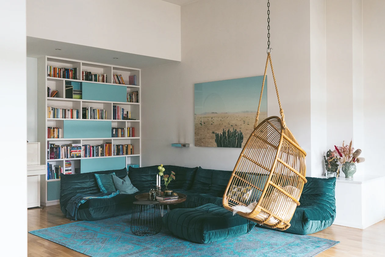 Living room with a teal velvet sofa, a hanging rattan chair and a built-in bookshelf. Photo: Tomo Yarmush